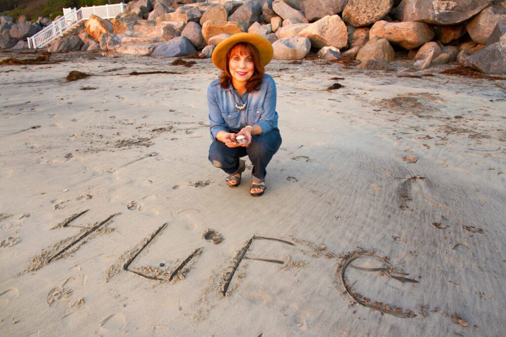 Bianca Lisonbee en una playa junto a un cartel grabado en la arena que anuncia "4LIFE"